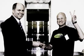 Vaalien häviäjä ja voittaja hymyssä suin. Keskellä sadan euron seteli.