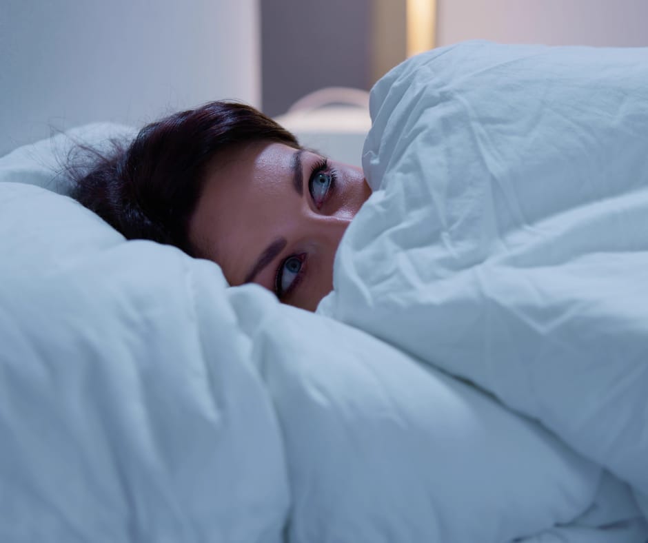 Kuvassa nainen makaa sängyssään yöllä. Hän on hereillä ja vähän peloissaan.
