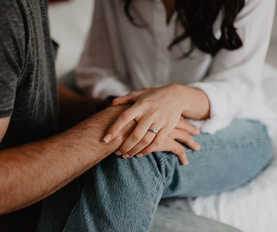 Kuvassa mies ja nainen istuu sängyllä ja pitävät toisiaan käsistä kiinni.