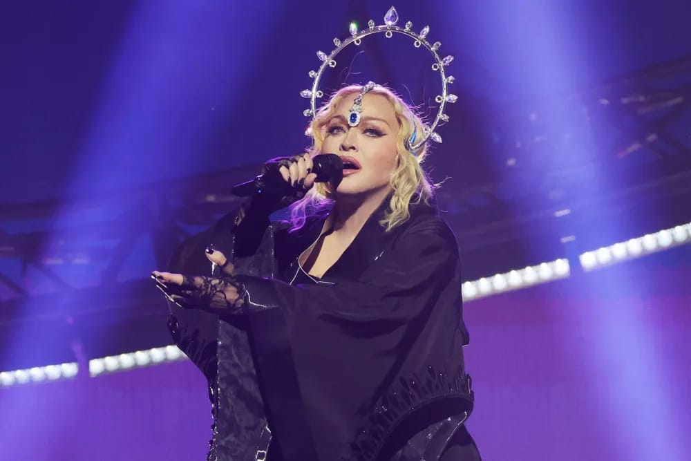 Madonna esiintyy lavalla mustassa asussa ja sädekehämäisessä päähineessä mikrofonin kanssa