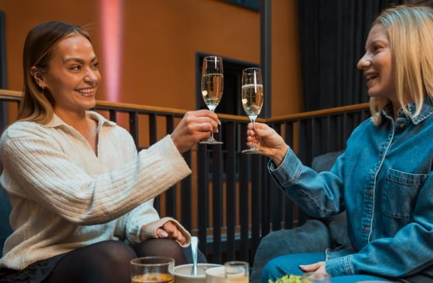 Naiset kippistelevät kuohuviinilasillisilla aamiaispöydässä.