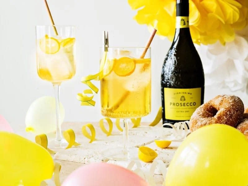 Laseissa vappujuomia. Taustalla serpentiinejä ja kuohuviinipullo. Edessä ilmapalloja.