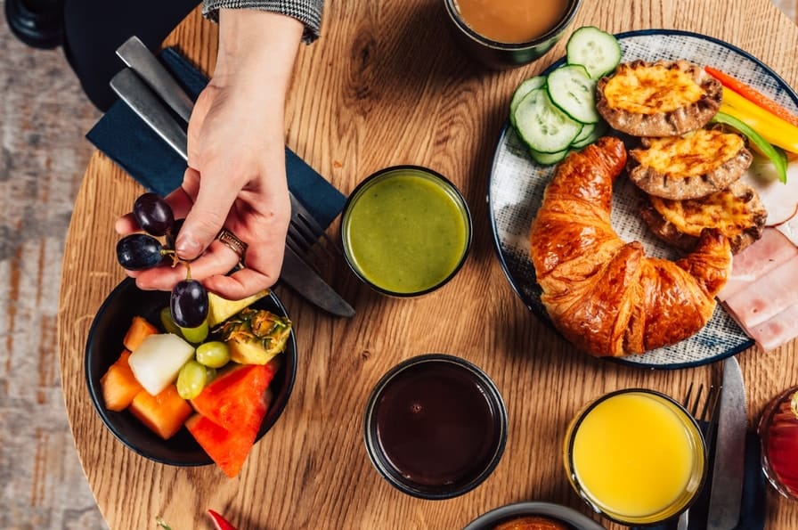 Pöydällä aamupalaa, kuten mehuja, croissantteja ja hedelmiä.