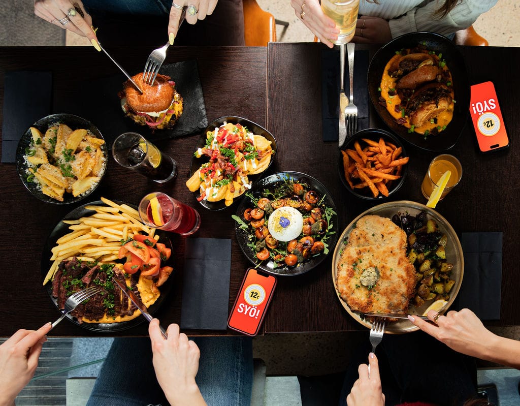 Ylhäältä kuvattu ravintolapöytä, jossa useita annoksia ja ihmisiä syömässä yhdessä.