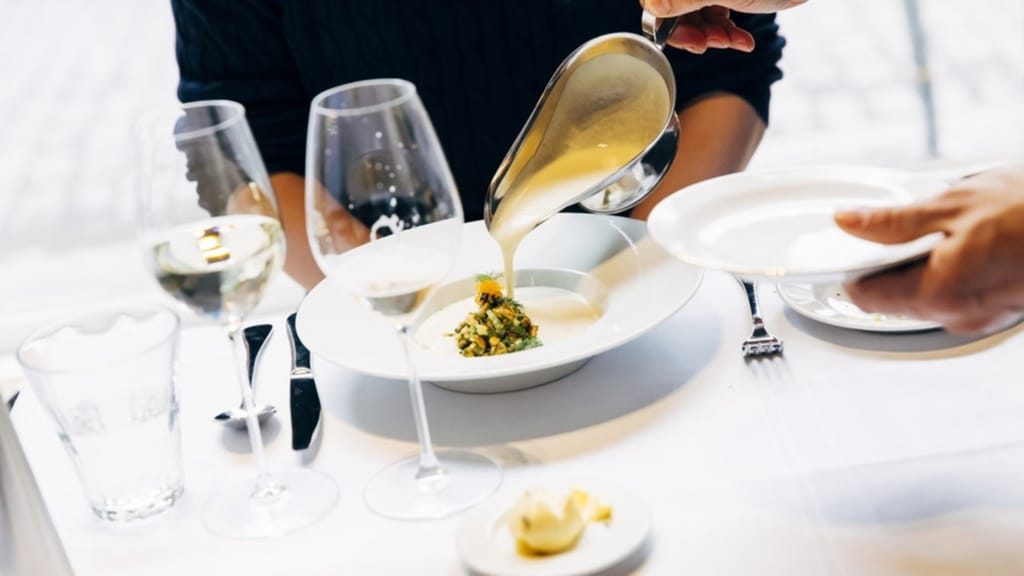 Tarjoilija kaataa kastiketta annokseen Vinkkelin ravintolapöydässä.