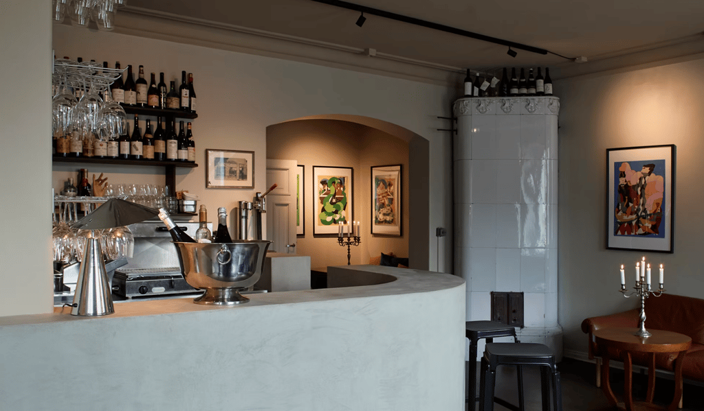 Viinibaari sisätiloissa, baaritiski, viinipullot hyllyillä ja kynttilöillä valaistu oleskelualue.