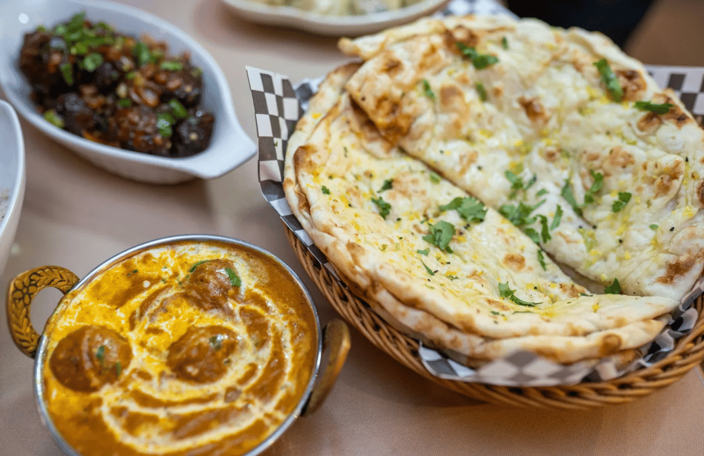 Intialainen curryannos ja naan-leipää korissa ravintolapöydässä.