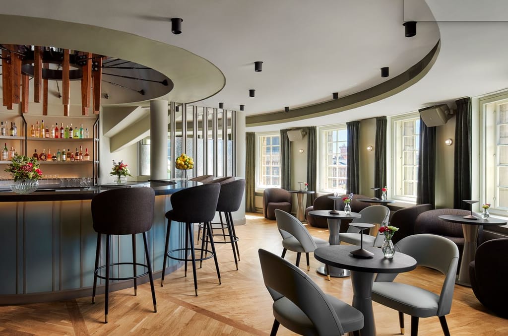 Tyylikäs baari- ja oleskelutila pyöreine pöytineen ja suurine ikkunoineen.