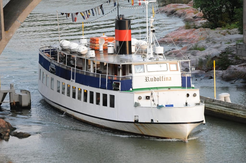 Ravintolalaiva Rudolfina kulkemassa saaristoväylällä kallioisen rannan vieressä.