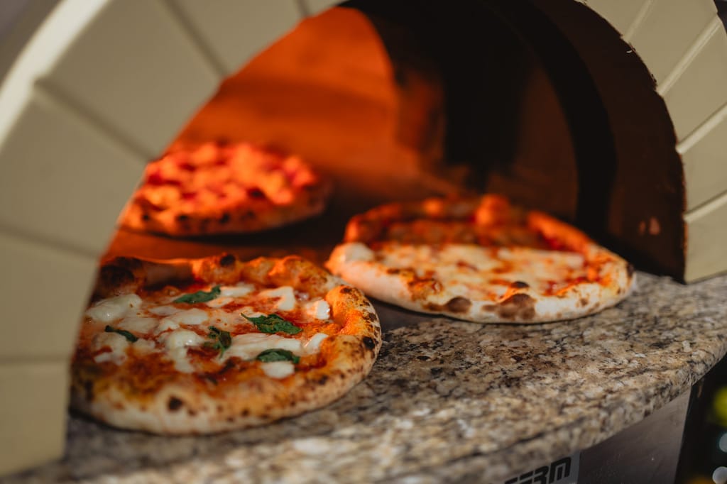 Pizzoja paistumassa kuumassa kiviuunissa, etualalla vastapaistettu margherita-pizza.