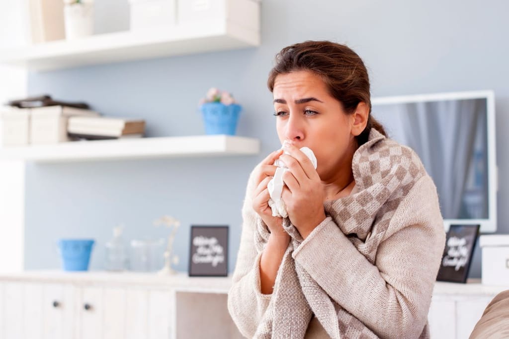 Nainen yskii kipeänä ja on pukeutuneena aamutakkiin ja yskii huivi kaulassa. 