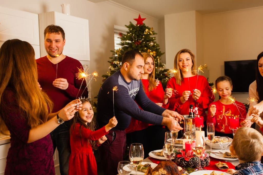 Jouluisesti pukeutunut perhe on kokoontuneena yhteen tähtisädetikkujen kanssa ja pöydässä on juhlajuomaa. Jouluinen yhteen kokoontuminen perheen ja suvun kesken. 