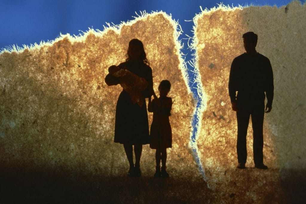 Abstrakti kuvituskuva kuvaamaan avioeroa. Kuvassa on äiti lapsi sylissä ja mies toisella puolella paperille piirrettynä, mutta paperi on revitty kahtia sinistä taustaa vasten.