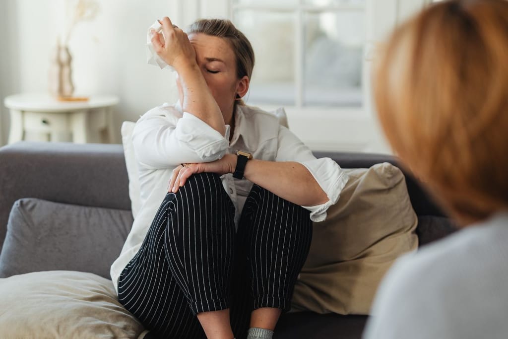 Nainen itkee terapeutille ja istuu vastapäätä sohvalla, pyyhkii nenäänsä 