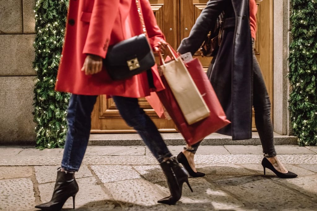 Naiset korkokengissä jouluostoksilla kaupungilla, jossa on vanha rakennuskanta. 