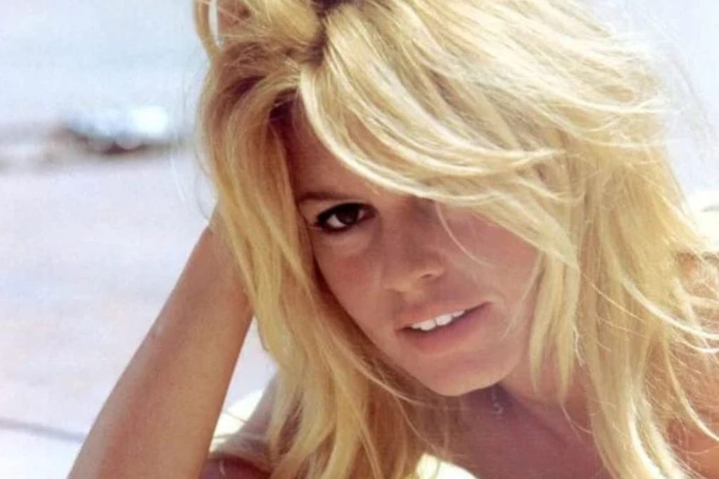 Brigitte Bardot nuorena vaaleraverikkönä kuvassa jossa makaa rannalla hyvässä valaistuksessa. Hän näyttää kauniilta ja poseeraa kameralle 