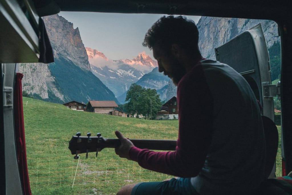 Mies soittaa kitaraa matkailuautossa vuoristossa siluettikuva