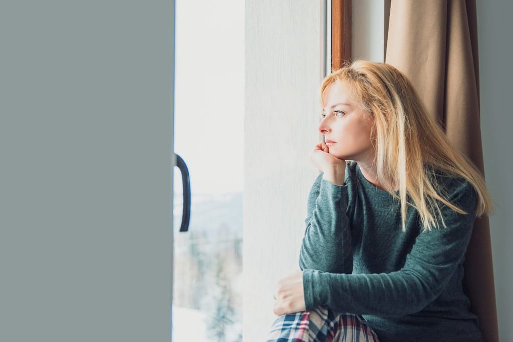 Nainen katsoo ikkunasta ulos vihreä paita päällään. Kuvituskuva, joka symboloi avioeroa ja yksin jäämistä. 