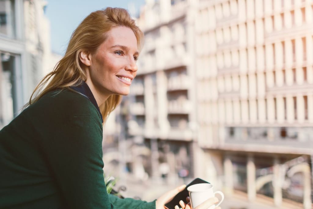 Nainen parvekkeella kahvikupin ja puhelimen kanssa