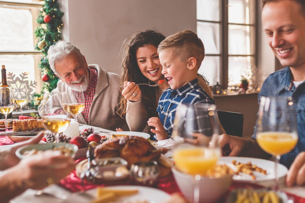 Perhe istuu joulupöydässä hyvässä hengessä syömässä. Jouluiset koristelut ja kaikkia naurattaa. 