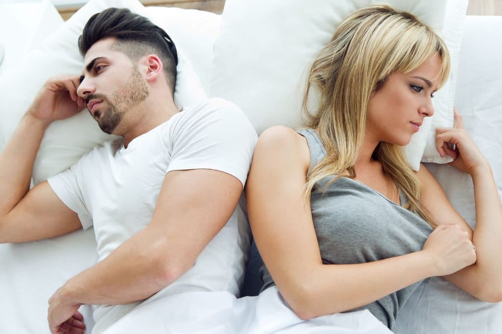 Pariskunta makaa riidoissa sängyssä valkeiden lakanoiden keskellä 