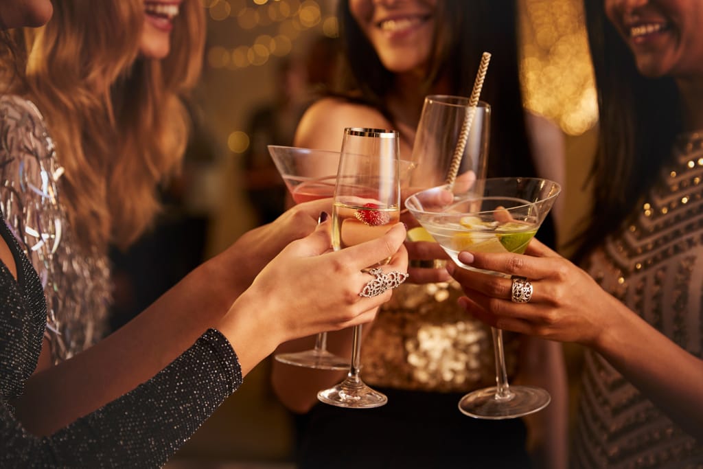 Naisilla on drinkit käsissään ja he skoolaavat jollekin. Kuvituskuva. 