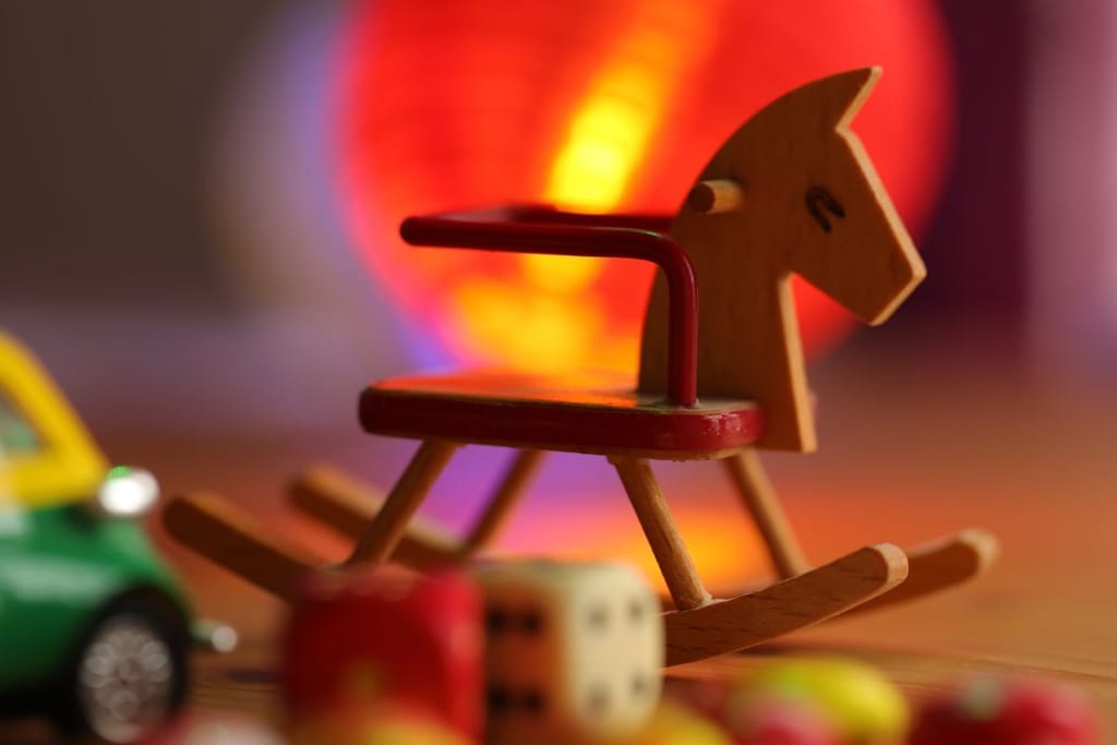 Vanhanaikainen puinen keinuhevonen, jossa on punainen kaide. Taustalla näkyy leluja ja punainen valaistus. 
