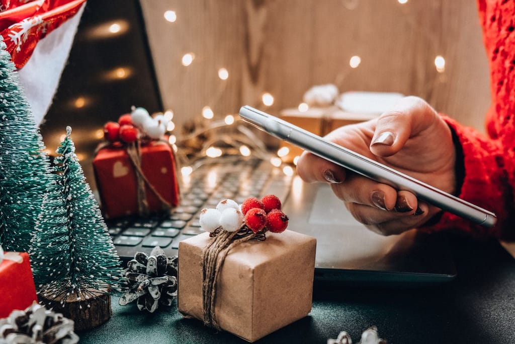 Nainen näppäilee kännykkää joululahjojen keskellä. Kuvituskuva. 