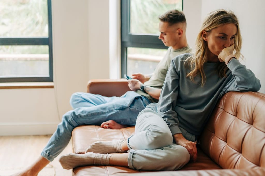 Nainen ja mies sohvalla konfliktitilanteessa. Nainen on kääntyneenä poispäin ja mies on keskittyneenä itseensä. Kuvituskuva artikkelille joka kuvastaa mustasukkaista vallankäyttöä.