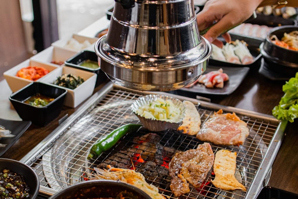 Korealainen BBQ-pöytä ravintolasta, jollaisia on myös Helsingissä. Kuvassa on barbeque-grilli, hiillos ja monta eri astiallista höysteitä ruokaa. 