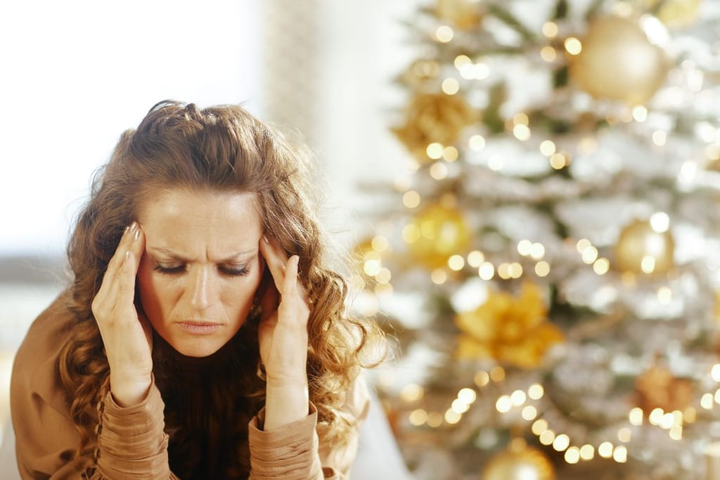 Nainen pitelee käsiä ohimoilla ja näyttää kärsivältä koristellun joulukuusen vieressä.