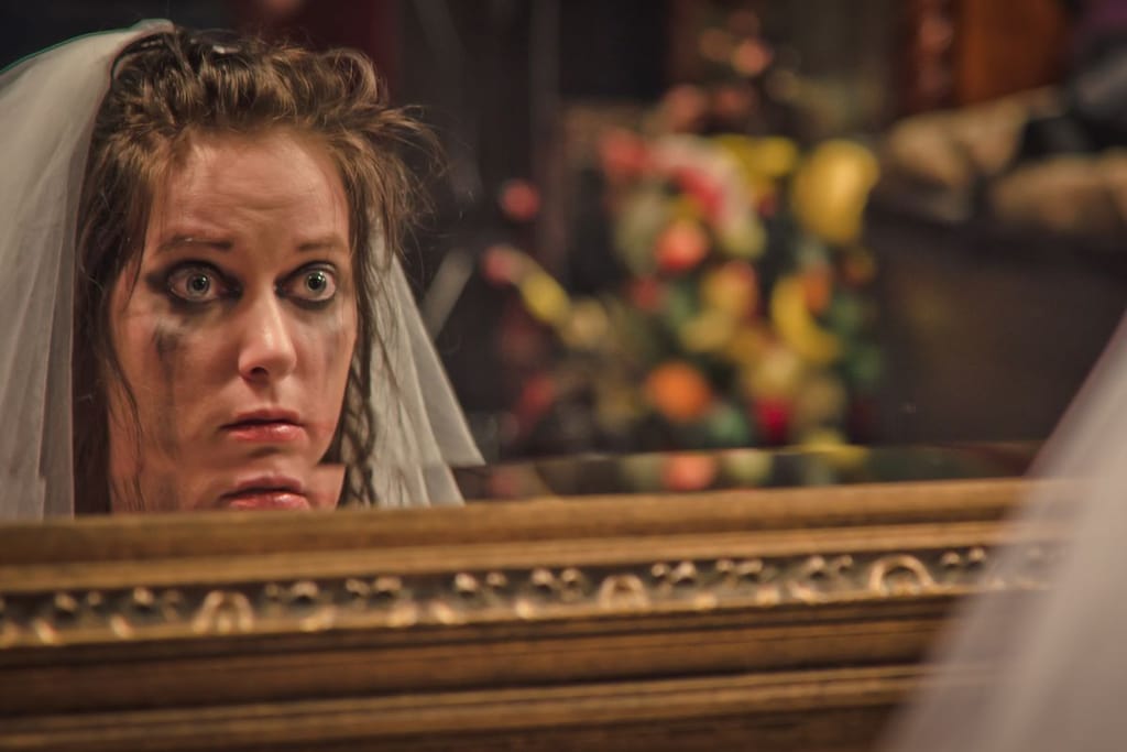 itkettynyt morsian katsoo itseään koristeellisesta peilistä huntu päässään rripsivärit poskilla.