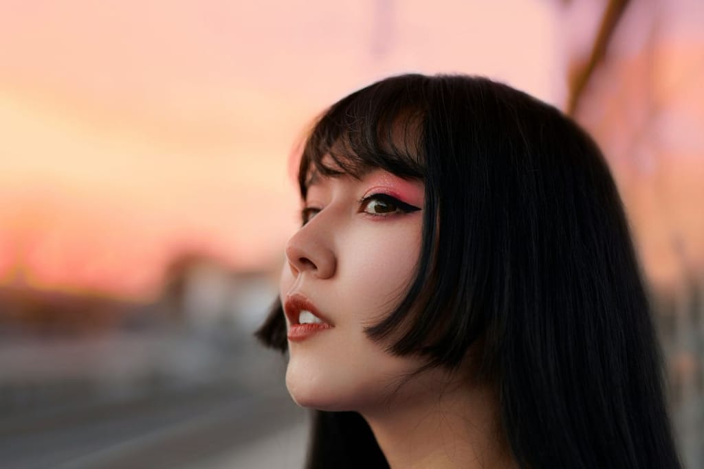 Mustatukkainen korealainen nainen uusvanhassa hiustyylissä katselee auringonlaskua. Vahvat rajaukset ja pinkki silmämeikki. Kuvituskuva. 
