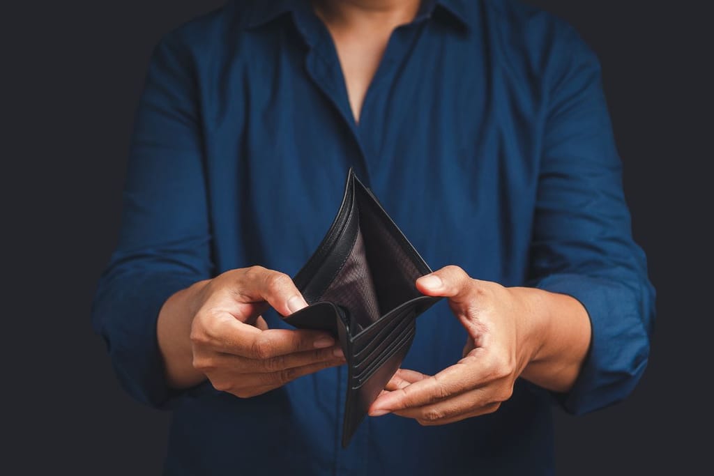 Mies näyttää nahkaista lompakkoa joka on tyhjä. Se on kuvituskuva teemalle rahattomuus jouluna.