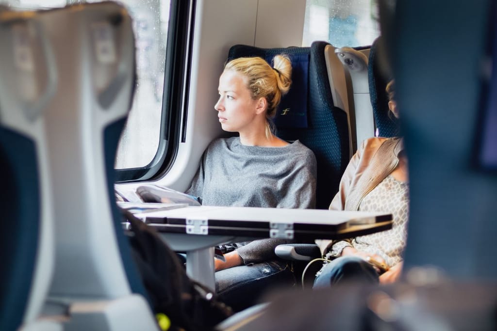 Nainen junassa. Kuvituskuva artikkeliin yksinäisyydestä. Nainen näyttää pohjoismaalaiselta ja istuu VR:n tapaisessa junassa.
