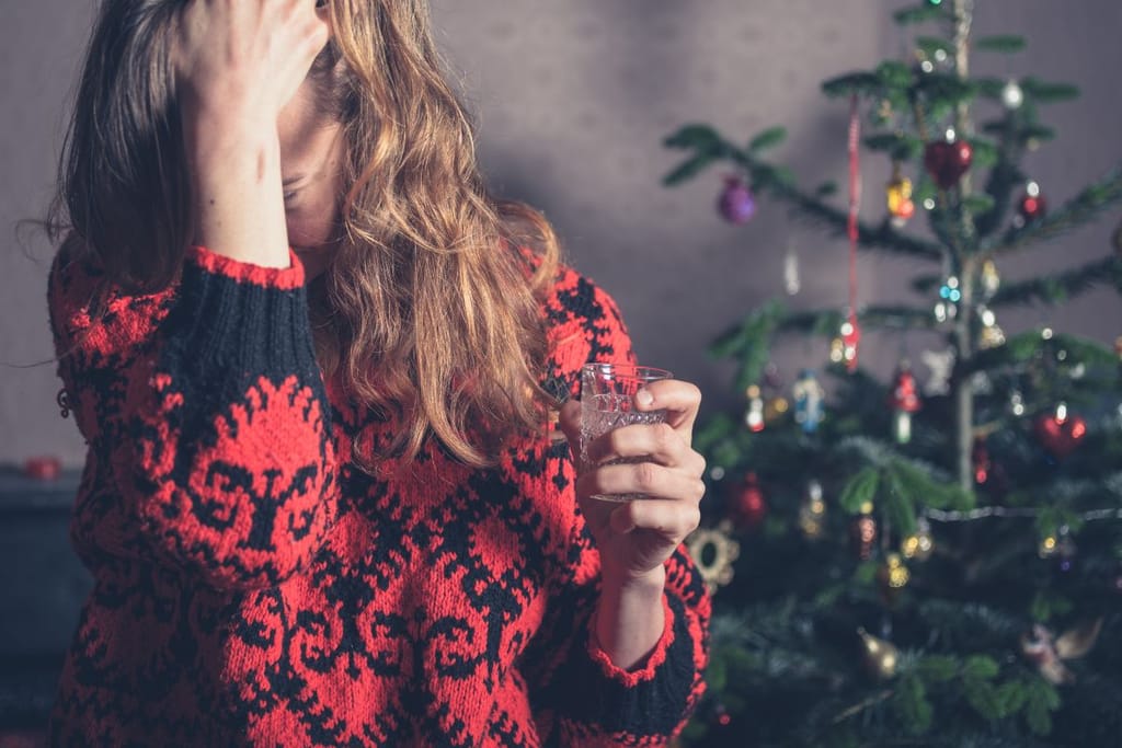 Nainen tuskailee lasi kädessä nuupahtaneen kuusen vierellä vesilasi kädessään. Hänellä on yllään jouluneule ja näyttää tuskastuneelta. Kuvituskuva artikkelille jouluköyhyydestä. 