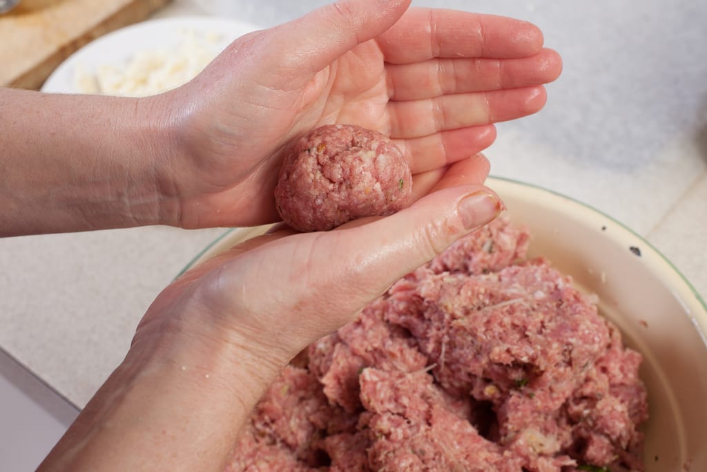 Lihapullien tekemistä. Raa'an lihapullan muotoilu käsissä ja taikina kulhossa