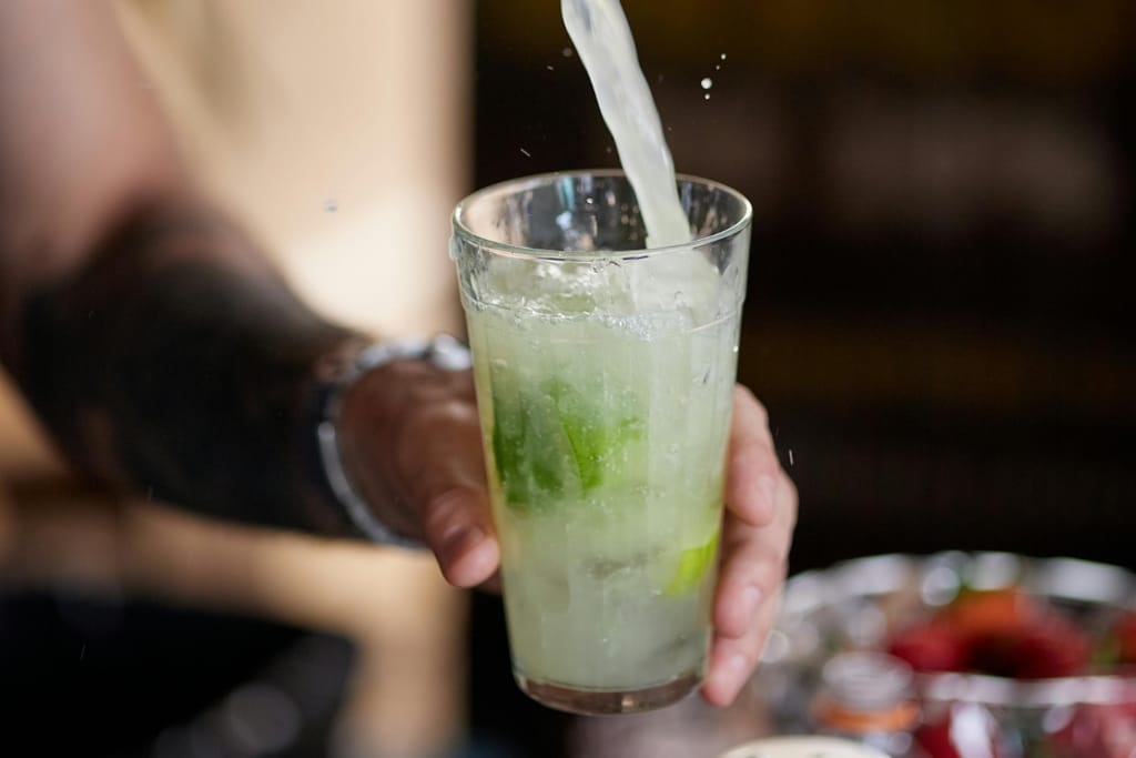 Baarimestari valmistaa suosittua mojito-drinkkiä ja kaataa juomaa lasiin.