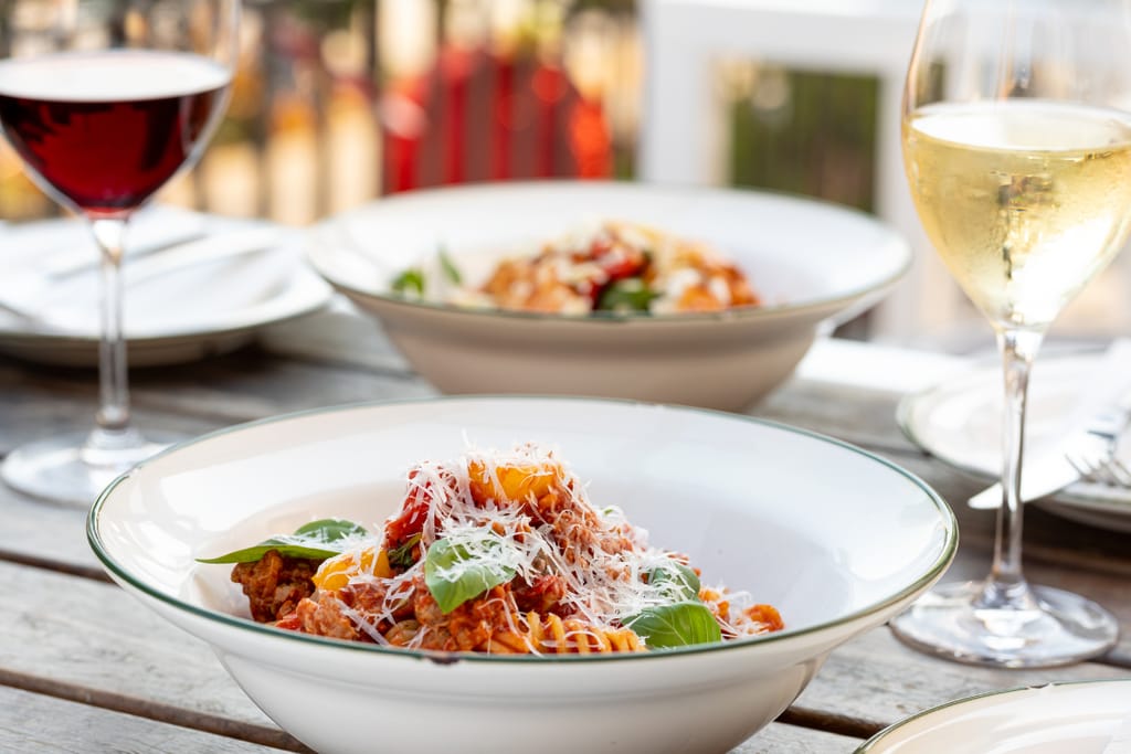 Kaksi annosta kierrepastaa lautasilla ja lasillisen puna- ja valkoviiniä.