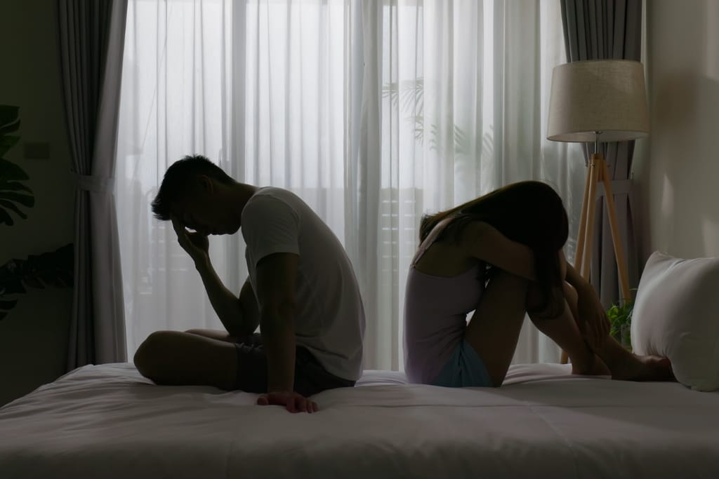 Kuvassa mies ja nainen istuvat sängyllä selät vastakkain ja nojaavat ominn käsiinsä. Molemmat ovat pettyneitä ja surullisia.