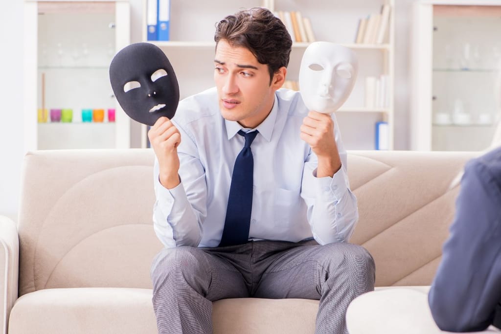 Mies istuu terapeuttisessa ympäristössä ja pitää käsissään kahta erilaista naamiota, mustaa ja valkoista. 