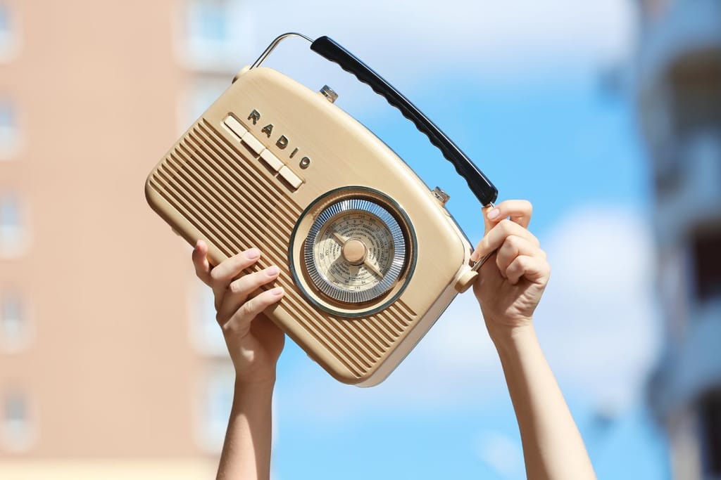 Henkilö pitelee käsissään kannettavaa radiota ulkona kirkasta taivasta vasten.
