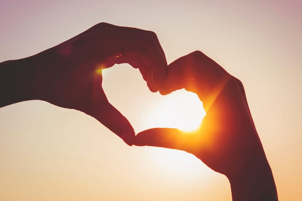 Kaksi ihmistä muodostavat käsillään sydämen auringonlaskua vasten.