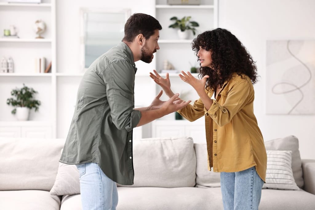 Kaksi ihmistä riitelee olohuoneessa. He seisovat vastakkain kädet kohotettuina. 