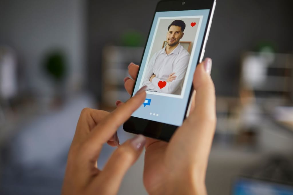 Kädet pitelevät älypuhelinta, jonka näytöllä näkyy deittisovelluksen profiilikuva miehestä ja sydänkuvakkeita.