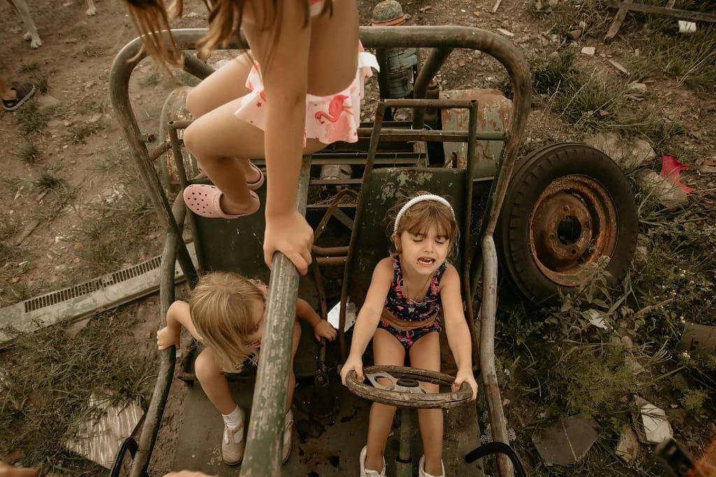 Lapset leikkivät romukasan keskellä. Yksi lapsista on ajavinaan autoa, ja toinen istuu vierellä kolmannen kiipeillessä. 