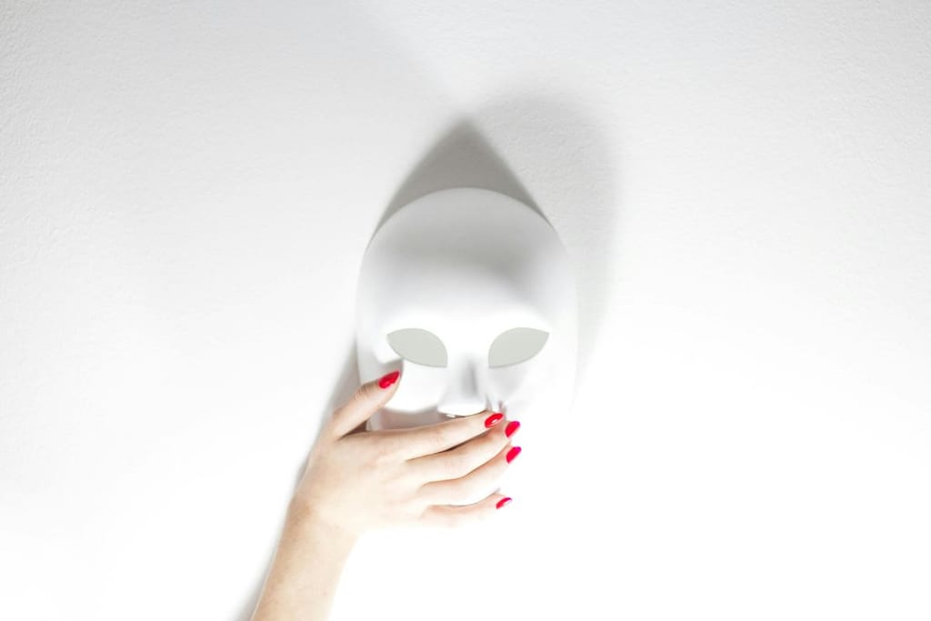 Valkoista taustaa vasten valkoinen naamio, jota symbolisena eleenä koskettaaa naisen käsi, jonka kynnet on lakattu punaisiksi.