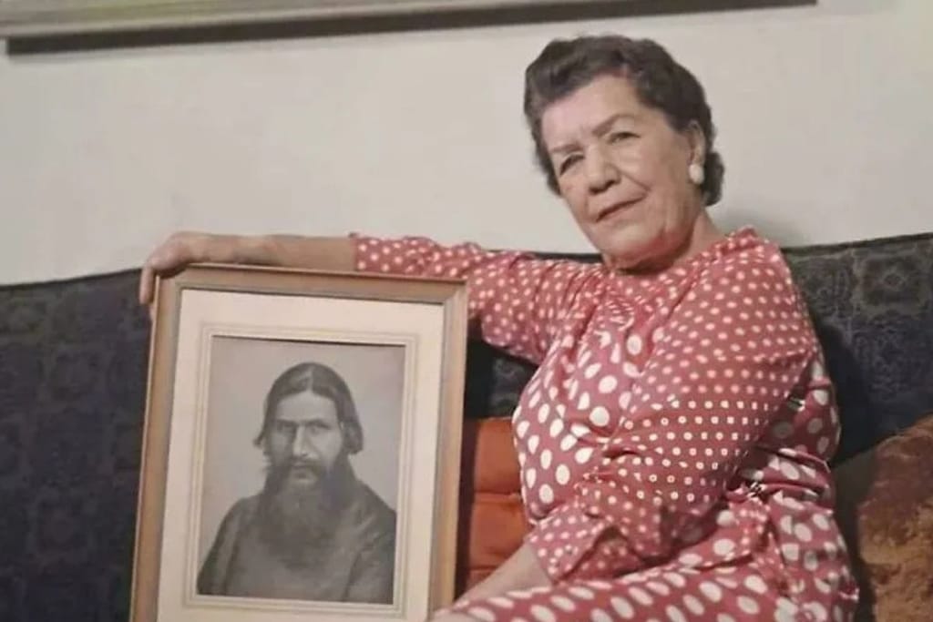 Vanhempi nainen esittelee ylpeänä isänsä muotokuvaa sohvalla valkoista seinää vasten. 