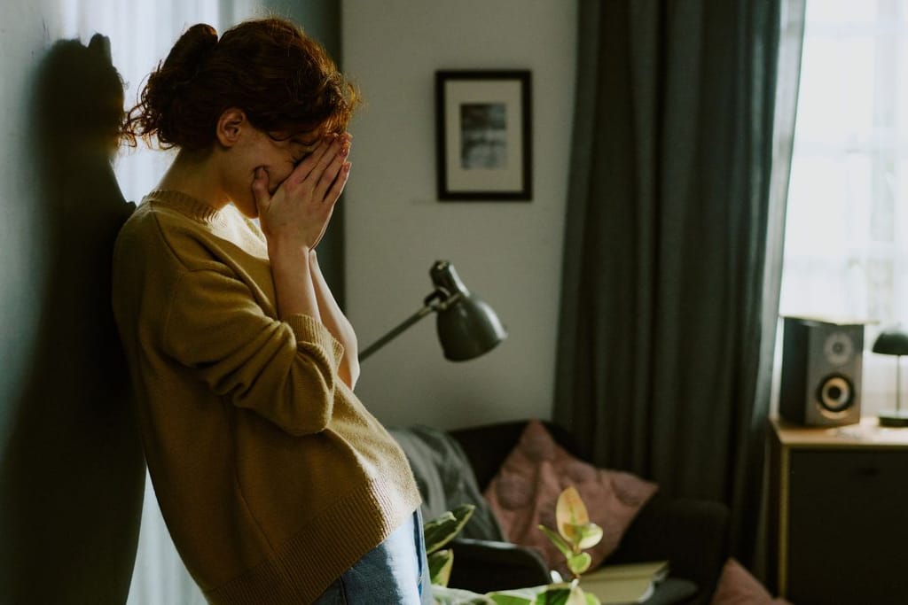 Nainen itkee seinää vasten ja on piilottanut kasvonsa käsillään. Hän vaikuttaa epätoivoiselta. 