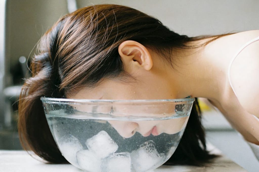 Henkilö upottaa kasvonsa kulholliseen vettä, jossa on jääpaloja. 